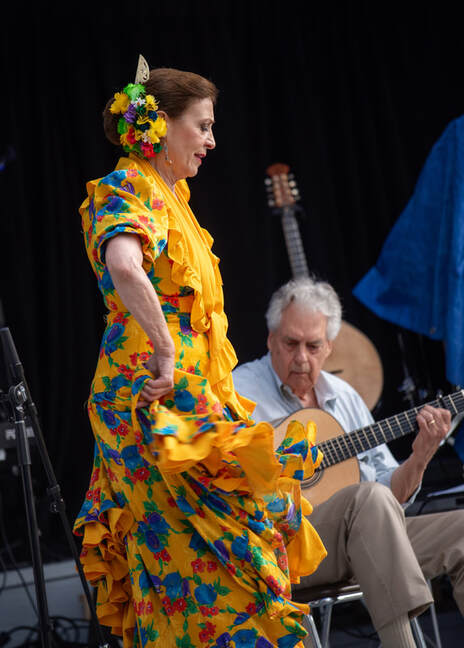 A lady in a yellow dress dancing next to a men playing a guitar 